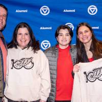Group of four posing for photo and smiling at camera, one holding up her custom sweatshirt